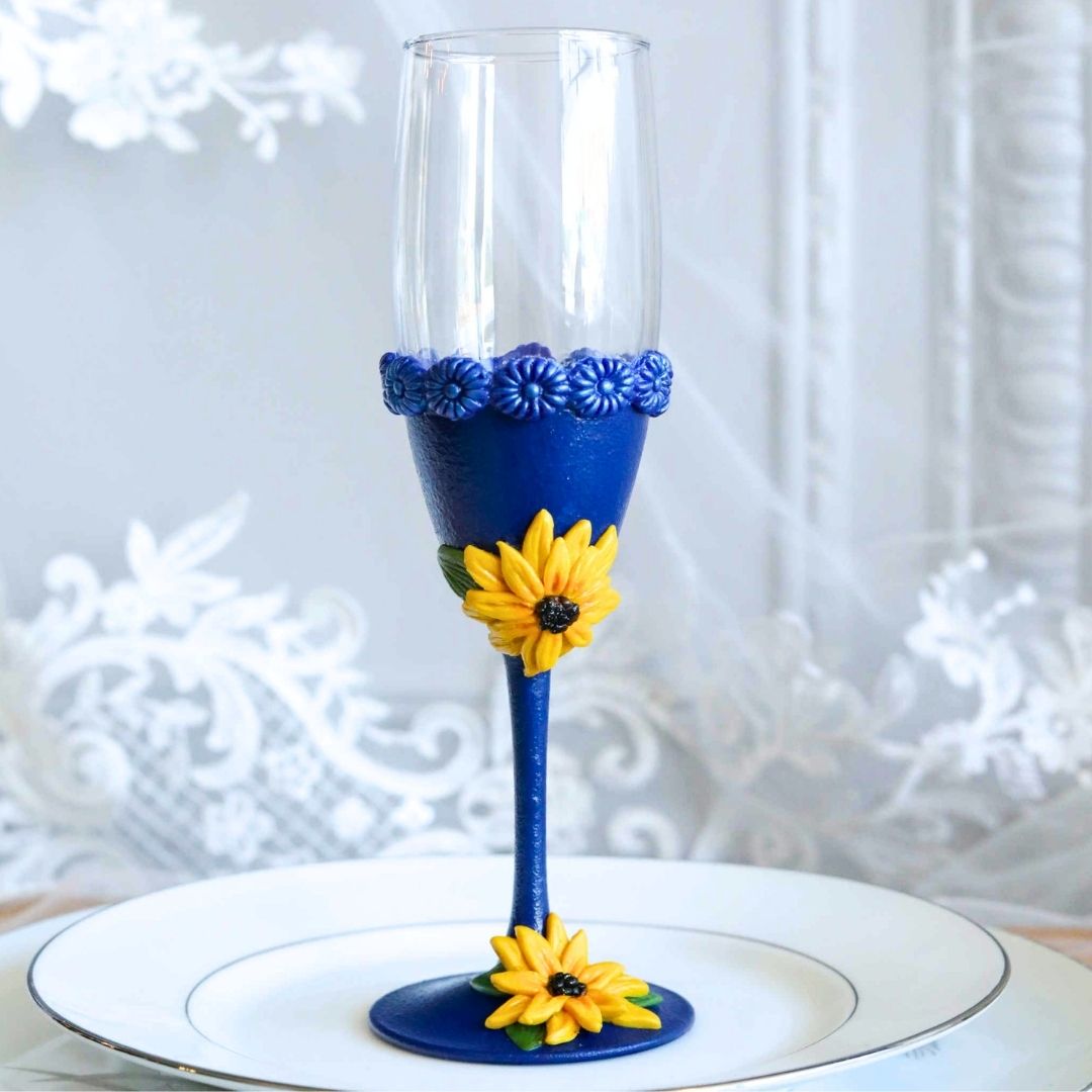 Hand sculpted blue and yellow sunflower wine glass displayed on a white plate with lace background, unique wedding gift or bridal shower gift