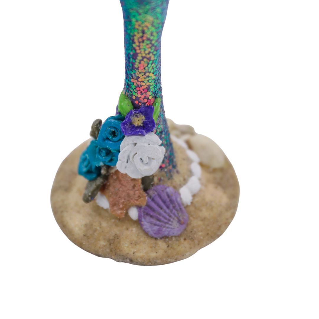 Close view of champagne flute base with real seashells, sand texture, and sculpted tropical flowers.