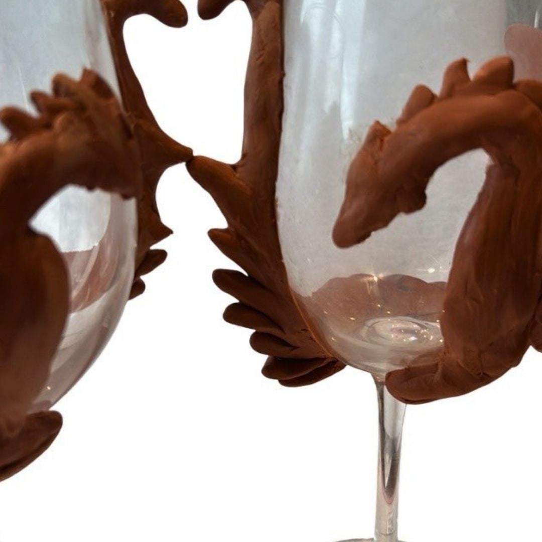 Hand sculpted green dragon wine glasses with polymer clay detailing, featuring textured dragon bodies and painted wings on clear stemware