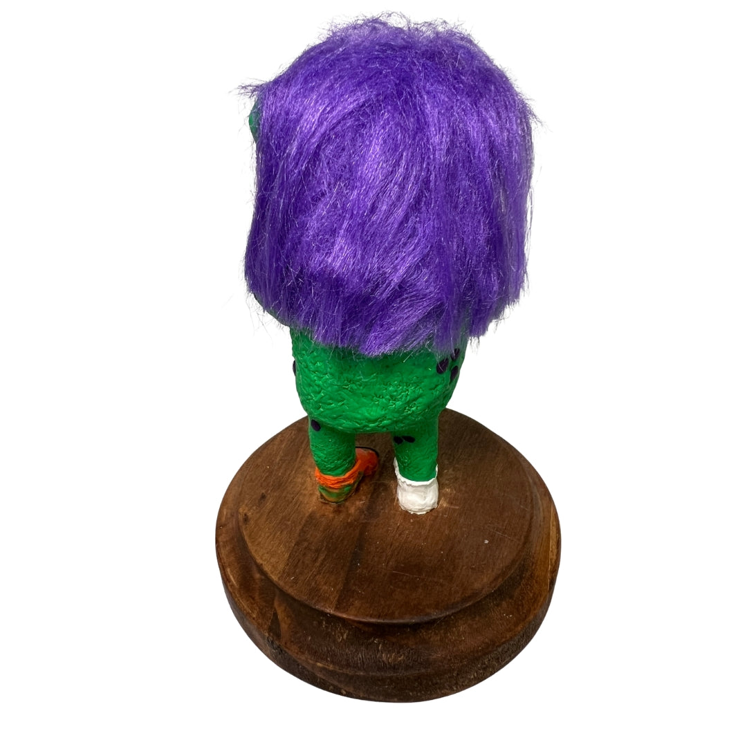 Back view of the Game On creature sculpture showing purple hair, textured green skin and wooden base.