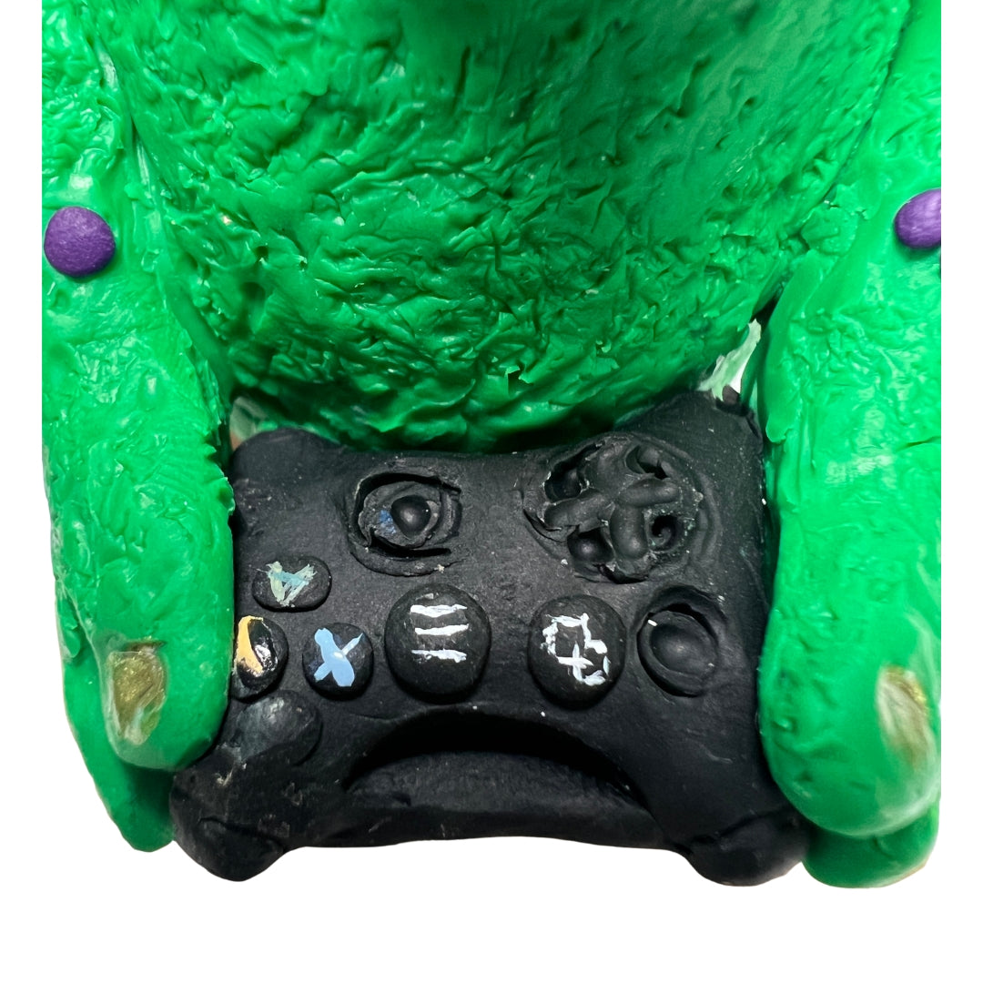 Close-up of the handmade black game controller held by the green Game On creature sculpture.