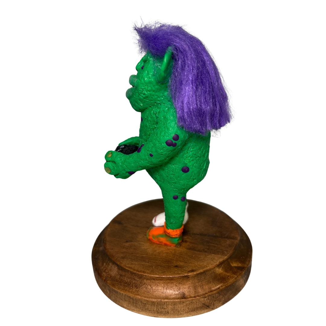 Left-side view of Game On holding a controller, with purple hair, green textured skin and an orange sock.
