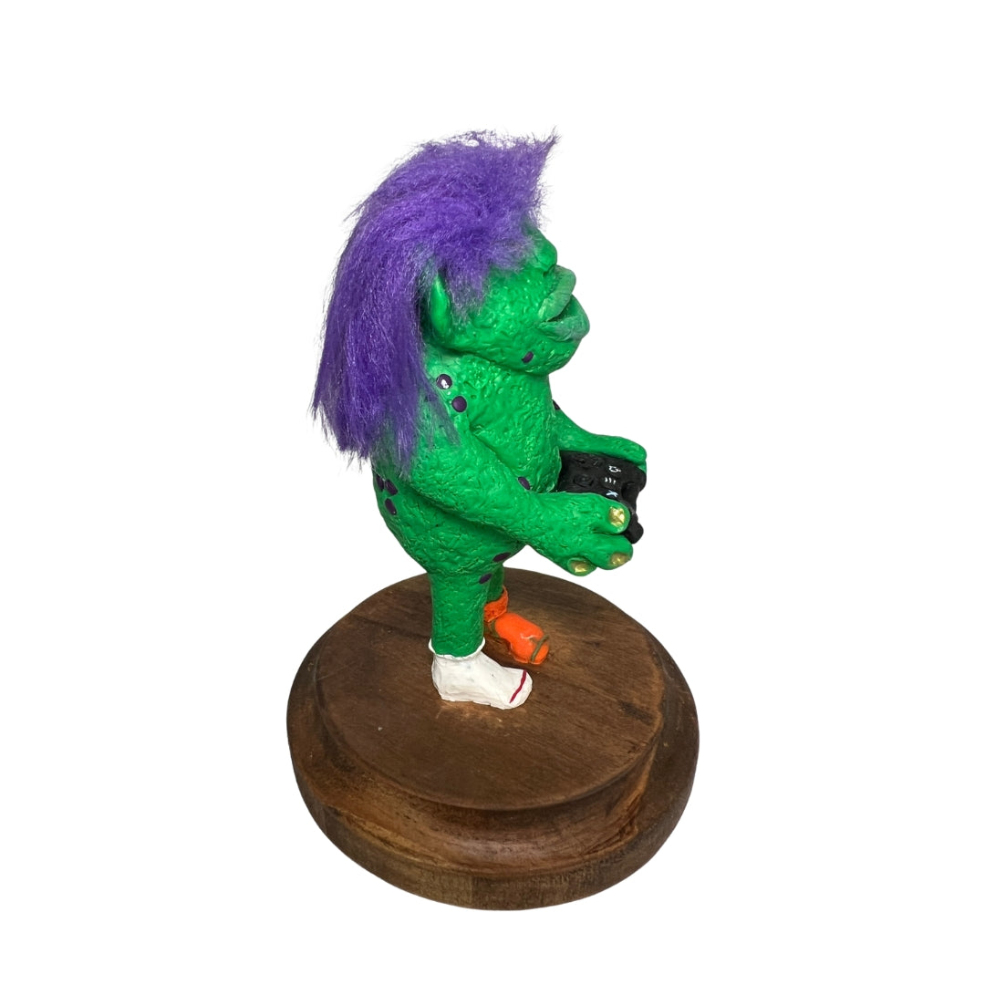 Right-side view of Game On holding a controller, with purple hair, green textured skin and a white sock.