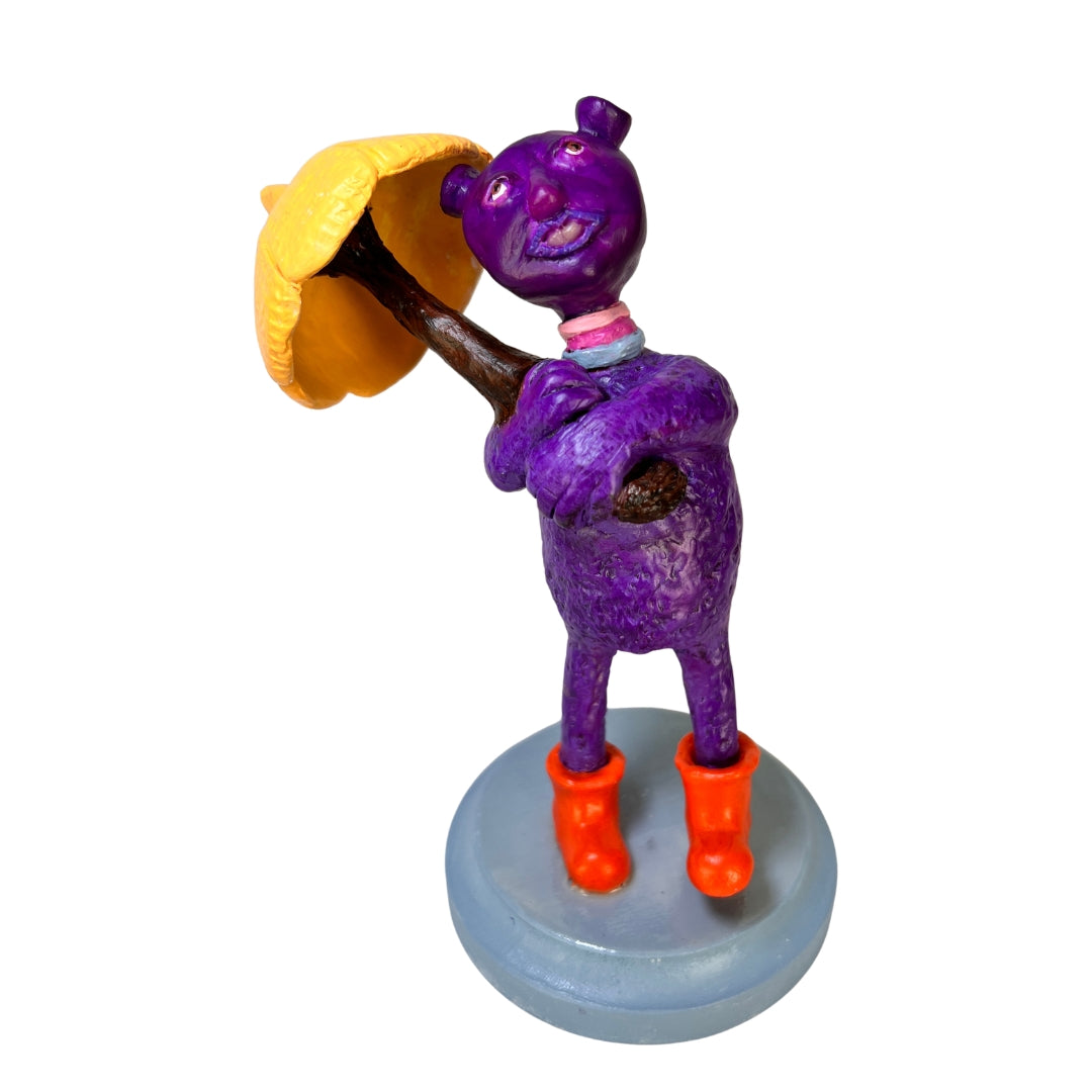 Purple Rainy Day Joy creature sculpture holding a yellow umbrella and wearing orange rain boots on a gray wooden base.