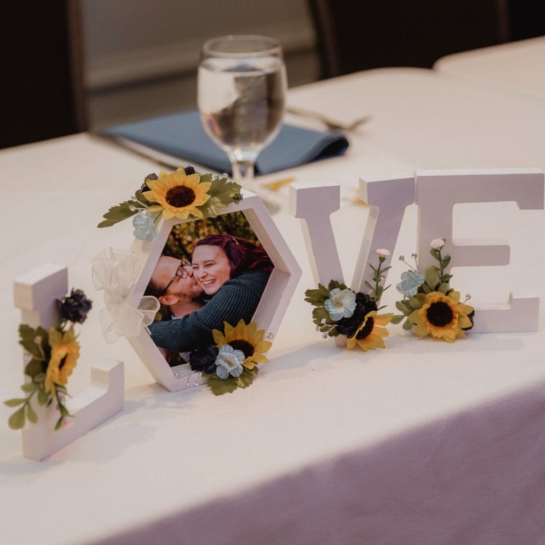 Sunflower LOVE photo centerpiece with hexagon picture frame, blue and yellow floral accents, and white letter decor on a wedding table display