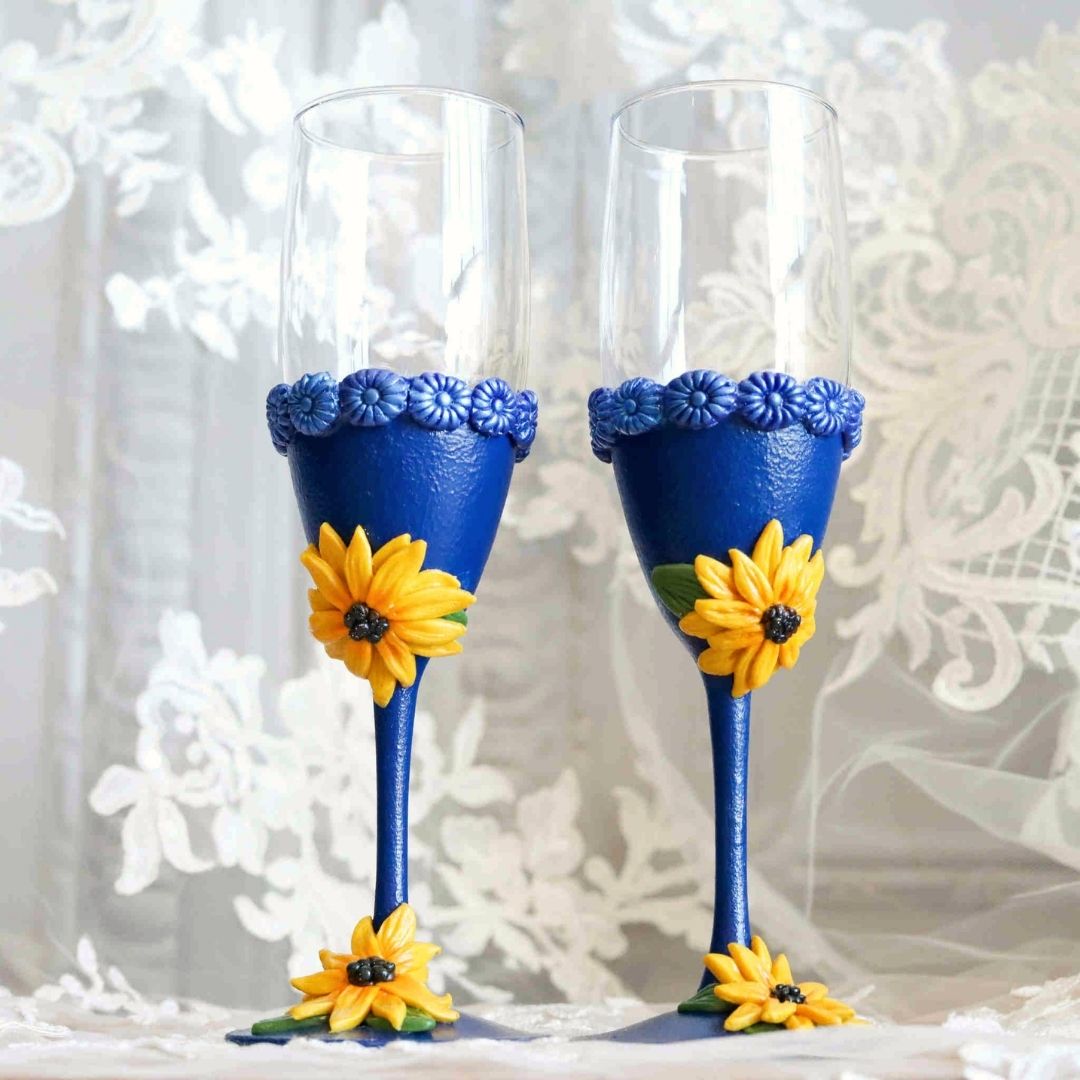 Hand sculpted blue champagne glasses with yellow sunflower details, bridal stemware set on lace background