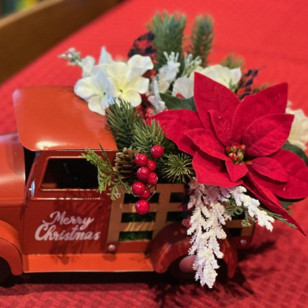 Main product photo of vintage red Christmas truck centerpiece with poinsettias, pinecones, berries, and winter greenery.
