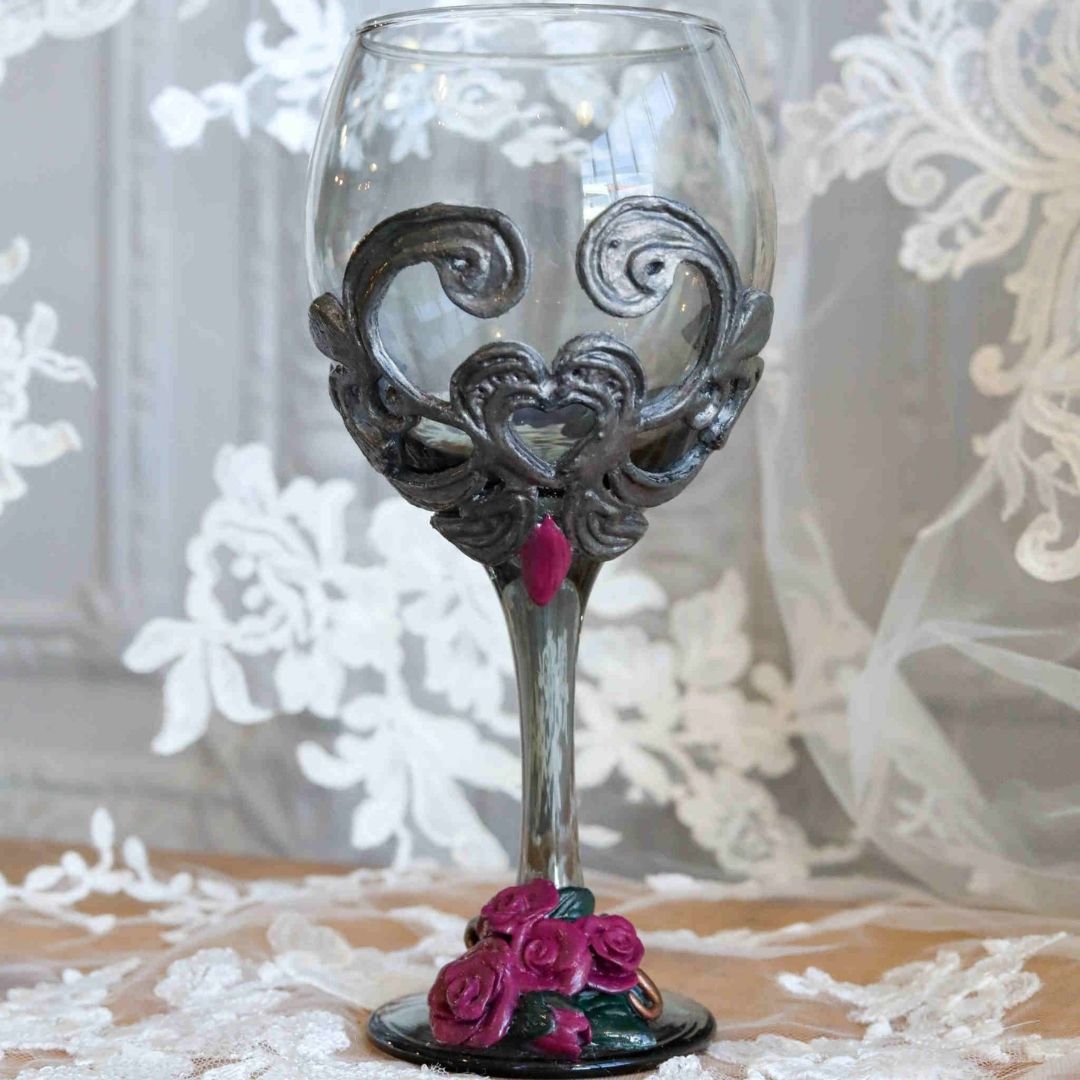 Victorian-inspired gothic wine glass with sculpted silver scrollwork and burgundy roses against a lace backdrop.