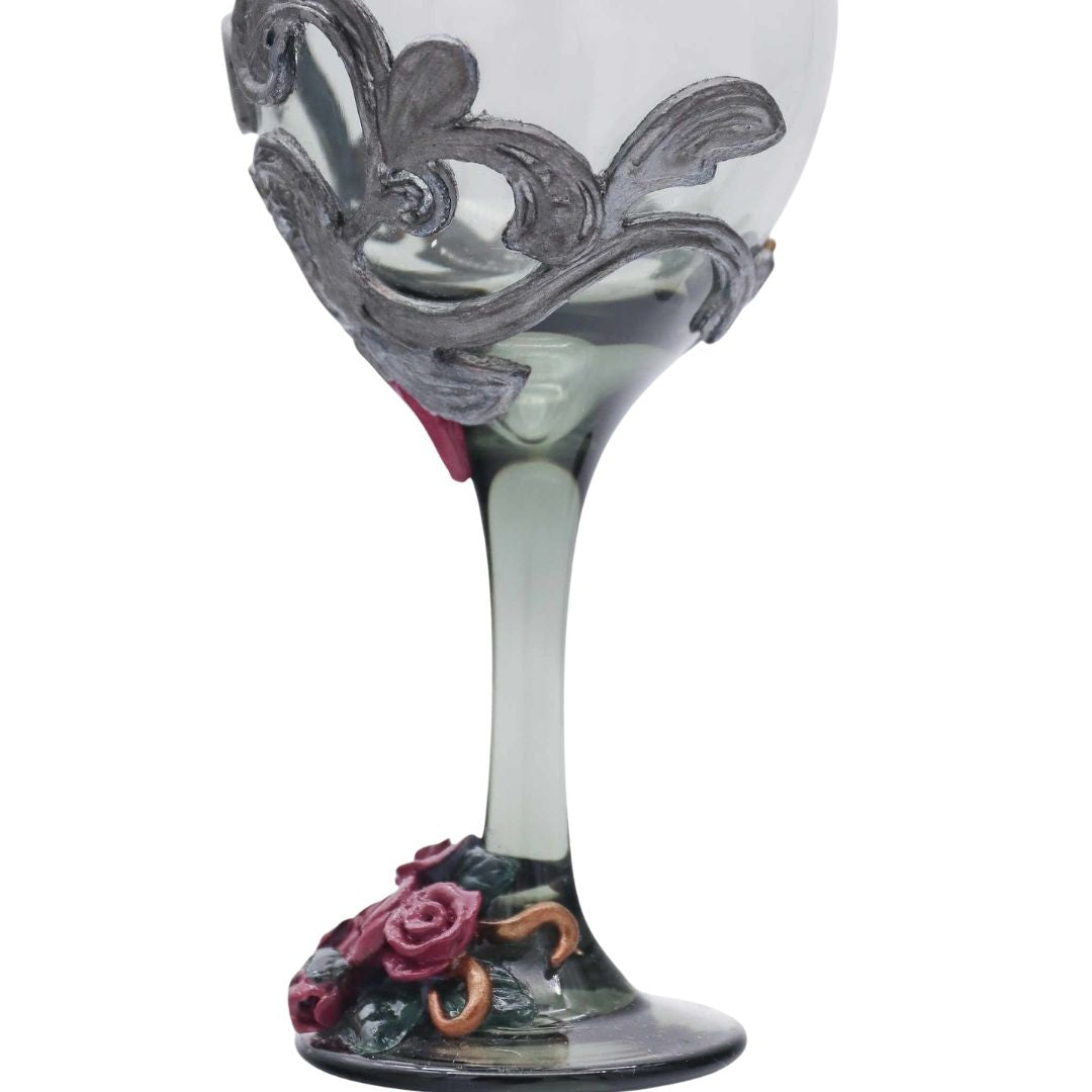 Close-up of a Victorian-inspired wine glass with silver scrollwork sculpting and burgundy roses around the stem and base.