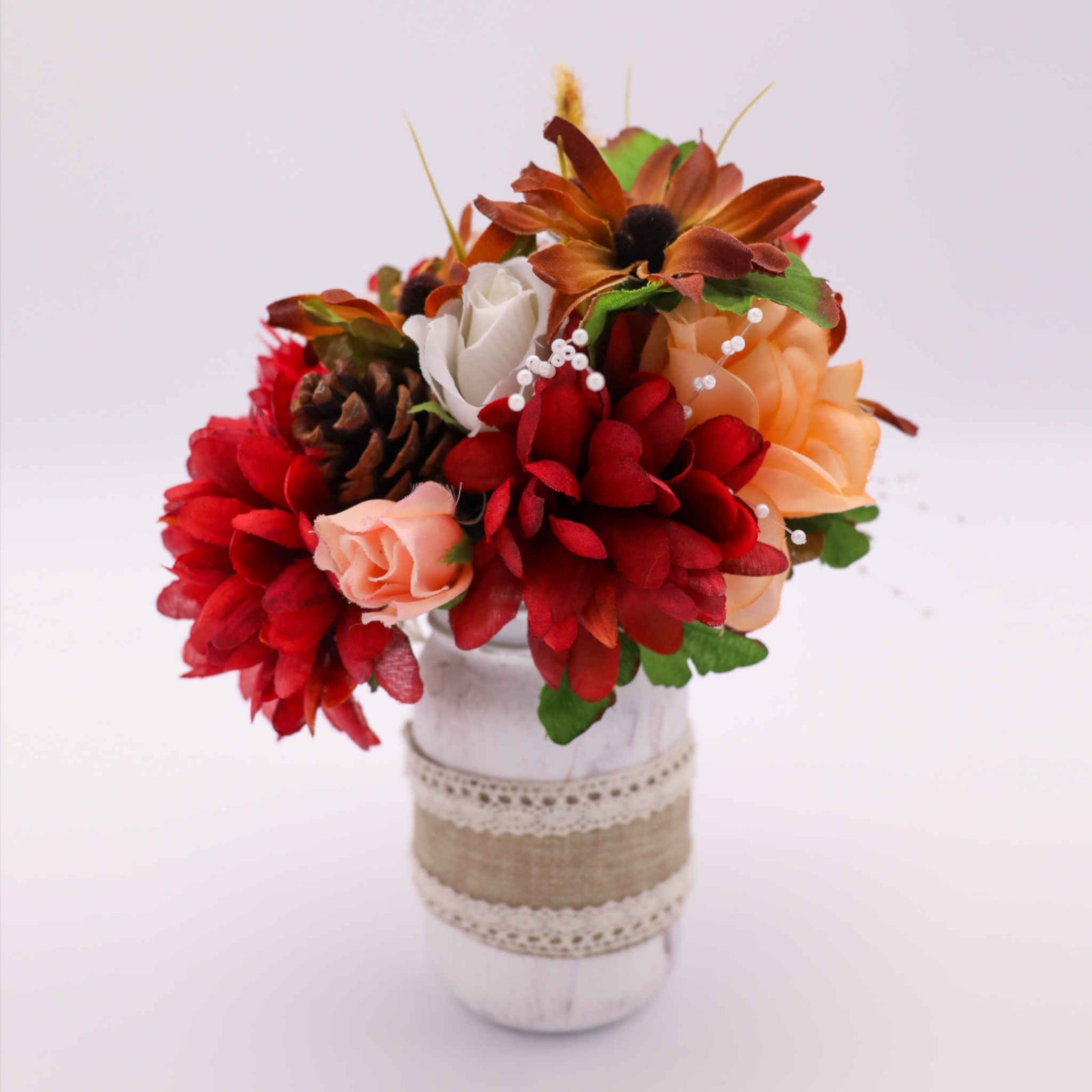 Add the feeling of Autumn to your celebration with our Autumn Mason Jar Centerpiece. This rustic mason jar centerpiece is the perfect compliment to an Autumn wedding. Adorned with burlap and lace, the mason jar holds seasonal silk flowers.