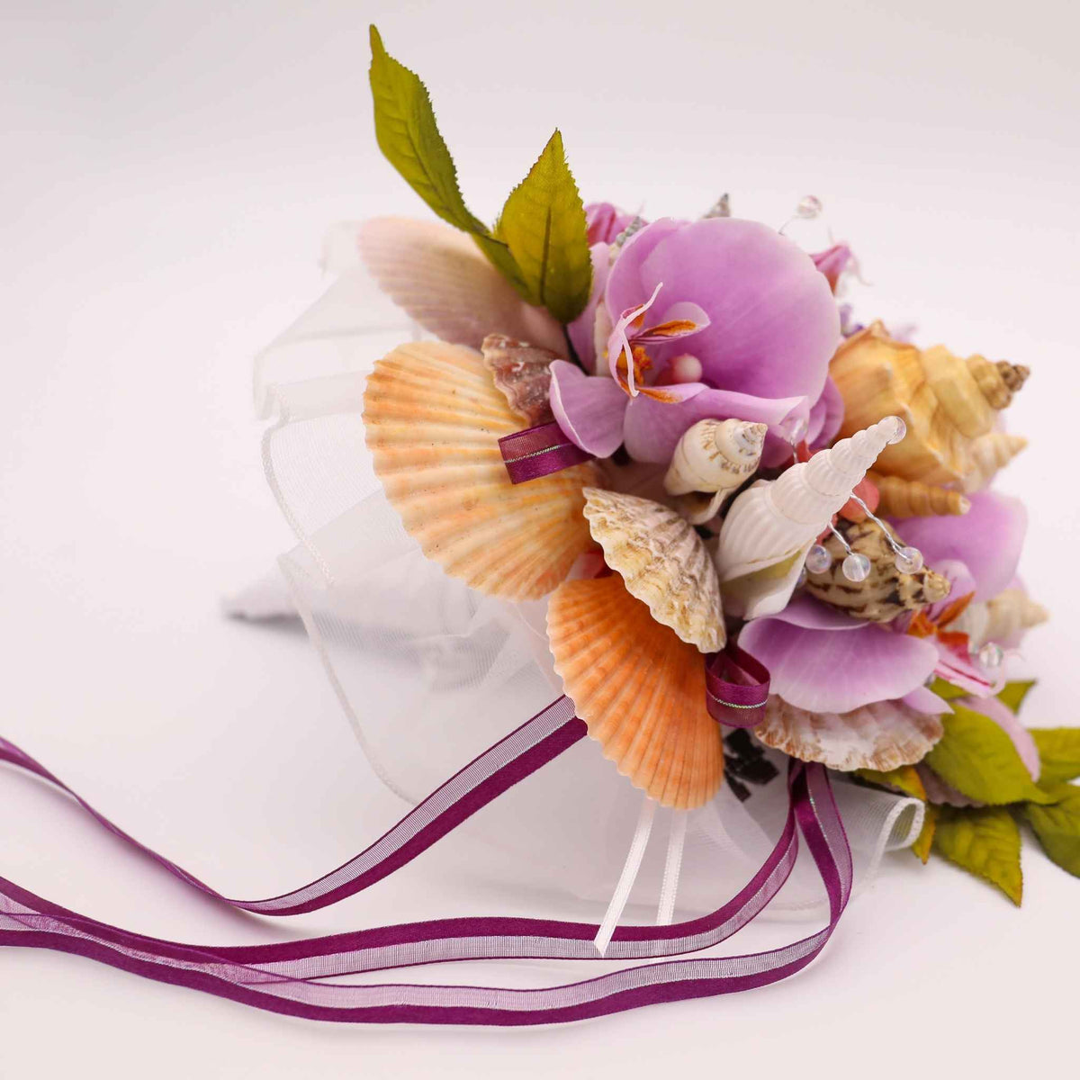 Bring the beauty of the beach to your tropical wedding ceremony. This cascading bouquet is adorned with various shells, silk orchids, ribbon, greenery and crystal bead stems.