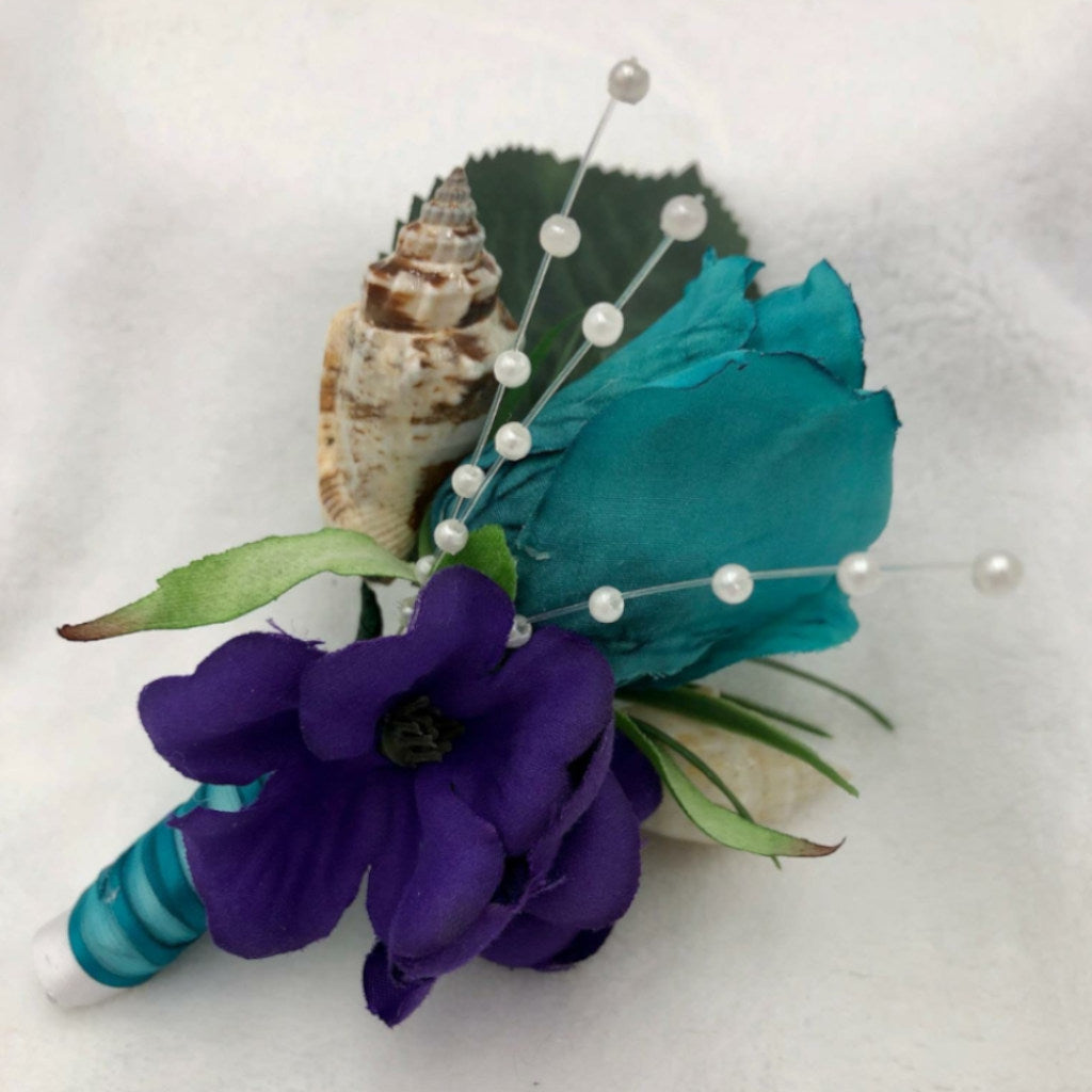 This tropical accessory is made with purple and turquoise flowers, accented with seashells and tiny pearls. The base of this boutonniere is wrapped in ribbon for an extra pop of color.