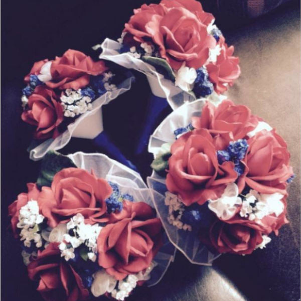 This round bouquet is lush with red silk flowers, accented with small blue and white flowers, and sits atop a plastic handle, wrapped in ribbon, finished with a simple lace collar.