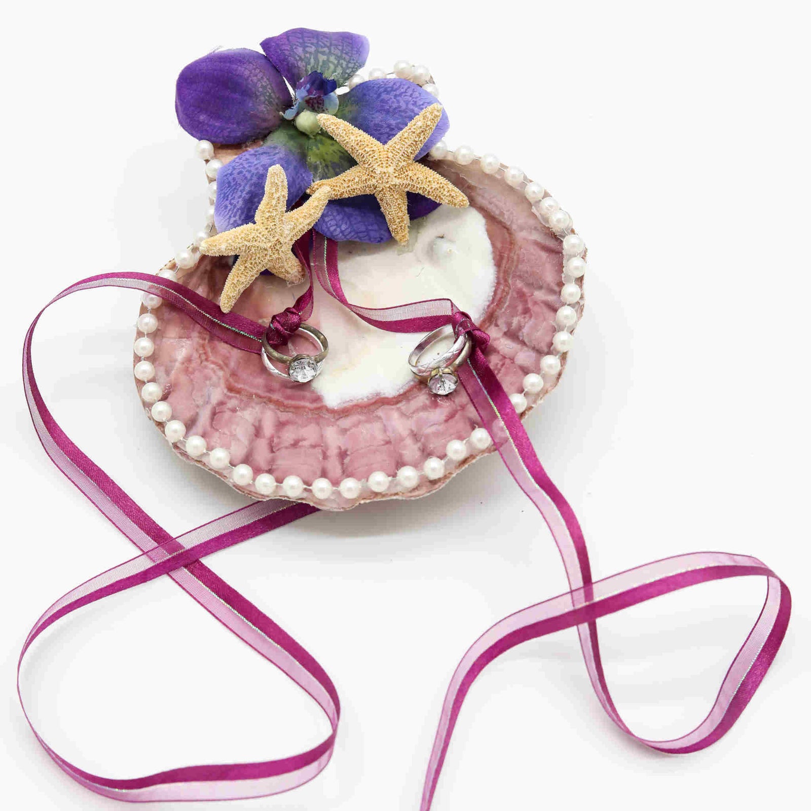 Have your wedding rings brought down the aisle in this beach inspired Scallop Shell Wedding Ring Holder. Made from a large, real shell, and decorated with pearl lace, small starfish, and a beautiful flower, this ring holder will keep your rings secure through a set of matching ribbons as its brought to the altar.
