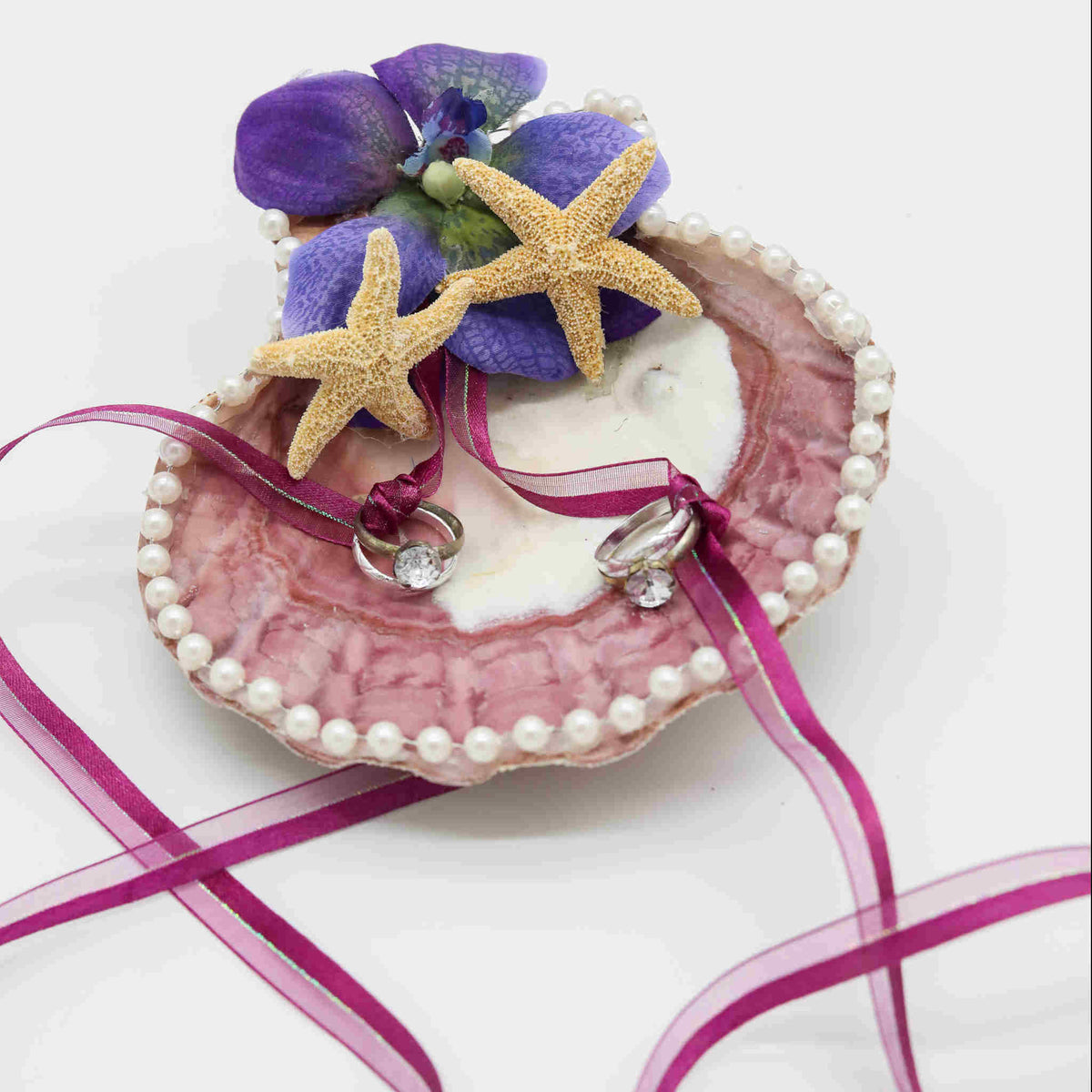 Have your wedding rings brought down the aisle in this beach inspired Scallop Shell Wedding Ring Holder. Made from a large, real shell, and decorated with pearl lace, small starfish, and a beautiful flower, this ring holder will keep your rings secure through a set of matching ribbons as its brought to the altar.