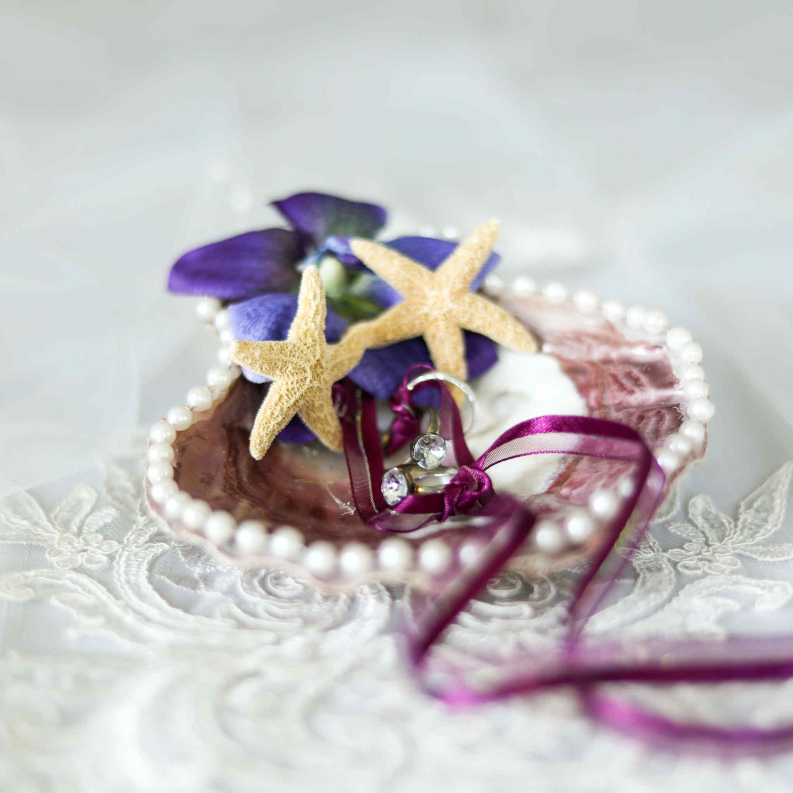 Have your wedding rings brought down the aisle in this beach inspired Scallop Shell Wedding Ring Holder. Made from a large, real shell, and decorated with pearl lace, small starfish, and a beautiful flower, this ring holder will keep your rings secure through a set of matching ribbons as its brought to the altar.