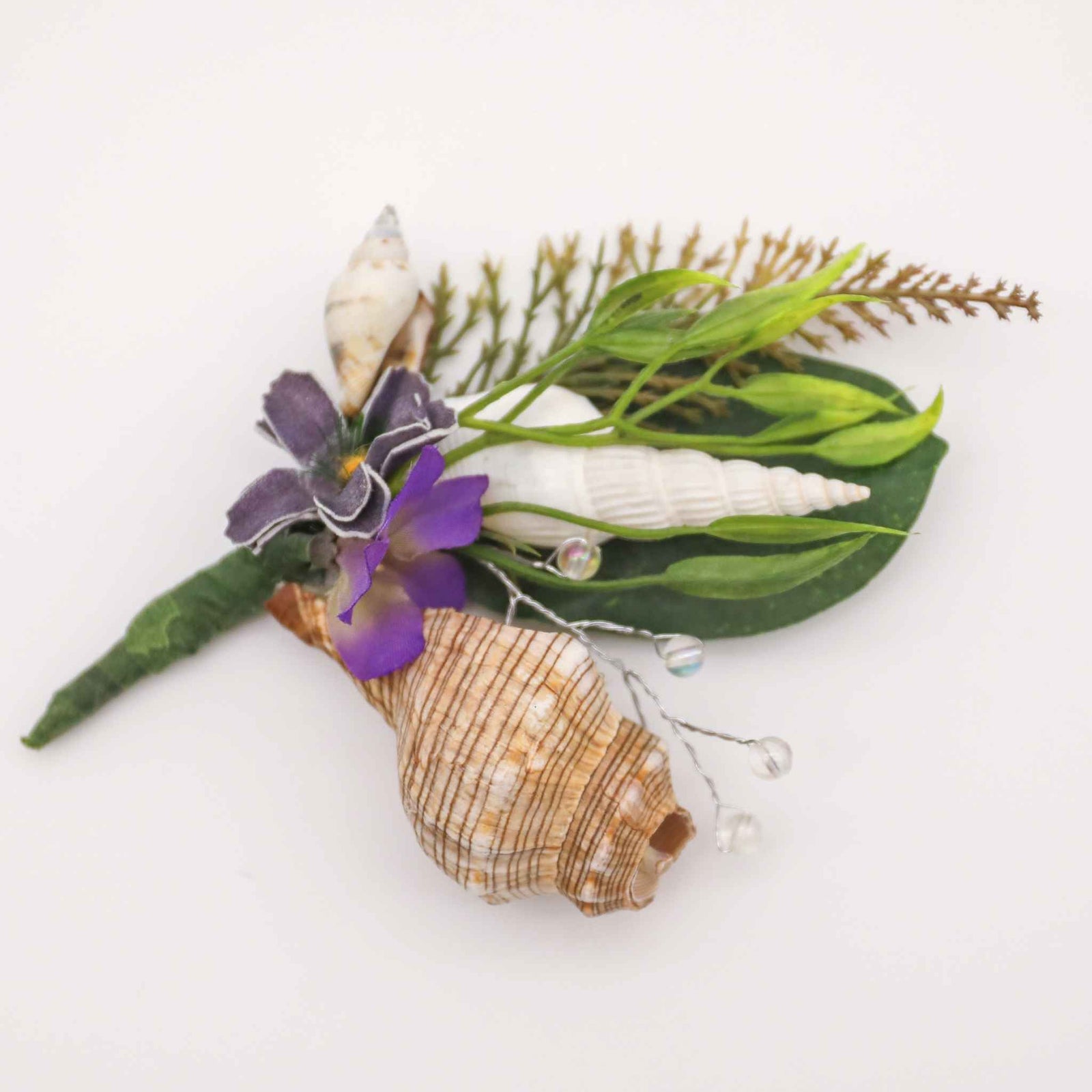 Bring the beach to your summer or tropical wedding ceremony. Set in greenery and adorned with cone shells and some small silk flowers, this boutonniere is a great accessory for any summer, beach, or tropical wedding.